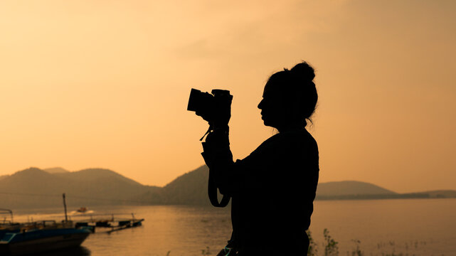 Silhouette of young woman photographer, taking pictures of the landscape at sunset