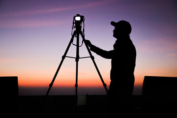 Silhouette of the photographer with tripod. Young Indian man taking photo with his camera during golden hour.