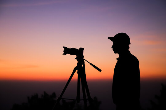 Silhouette of the photographer with tripod. Young Indian man taking photo with his camera during golden hour.