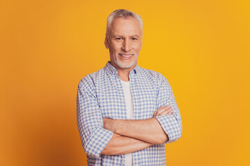 Self confident man keeps hands crossed looks at camera isolated over yellow background