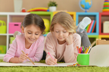 Two cute little girls drawing with pencils while lying on floor