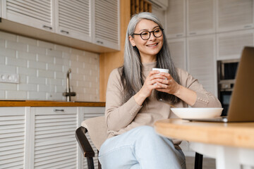 Mature smiling woman drinking coffee while working with laptop