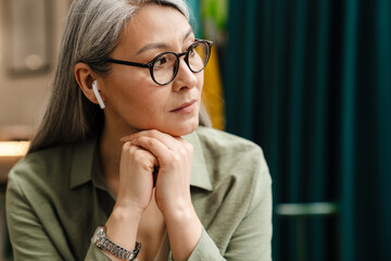 Mature grey woman listening music with earphones while sitting in cafe