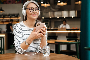 Mature smiling woman listening music with headphones and cellphone