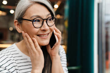 Mature woman smiling and talking on cellphone in cafe indoors