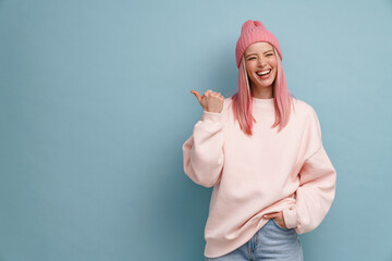 Young woman wearing pink hat laughing and pointing finger aside