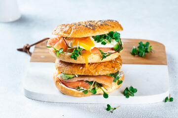 Healthy freshly baked bagel filled with salmon, microgreen, avocado and egg. Served on white desk. Sandwich with salmon. Healthy breakfast.