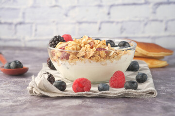 Granola and berries in bowl on pink background 