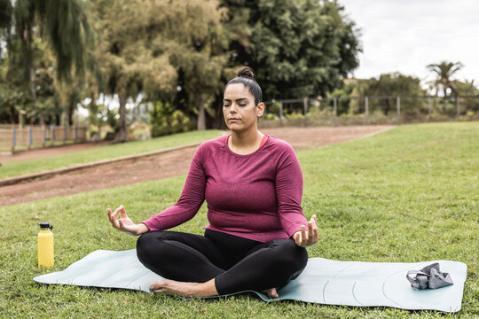 Curvy woman doing yoga session outdoor at city park - Focus on face