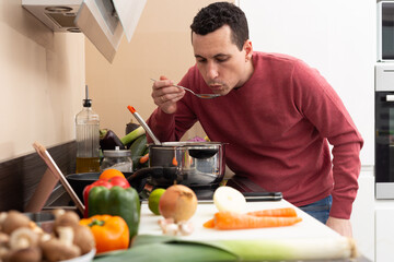 Man wearing an apron cooking at home in a modern kitchen vegetarian and vegan food looking at a tablet. Healthy recipe.