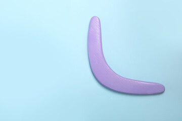 Lilac wooden boomerang on light blue background, top view. Space for text