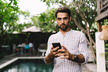 Handsome young male blogger using smartphone on terrace