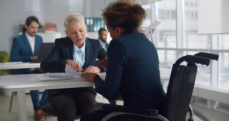 Caucasian businesswoman in wheelchair consulting colleague in office