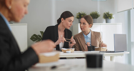 Business people sitting at table in front of laptop and having lunch together in office