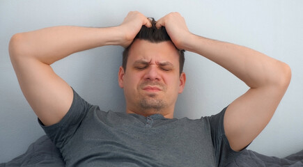 Portrait of young man with hangover waking up in bed feeling terrible headache looking at camera....
