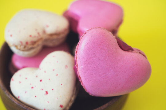 Macaroons biscuits on a yellow background. French biscuits in gift box. Sweet macarons in a gift box. Traditional French colorful macarons. Valentine's day gift. Heart shaped pink macarons.