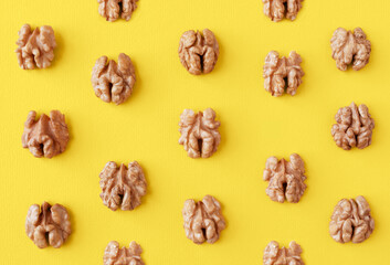 Obraz premium Halves of walnuts on a yellow trendy color 2021 year background, pattern, top view.