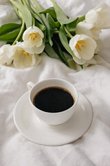 Cup of coffee and white tulips on the white bed