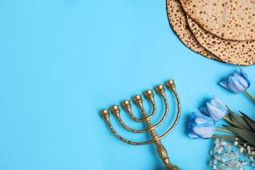 Tasty matzos, flowers and menorah on light blue background, flat lay with space for text. Passover (Pesach) celebration