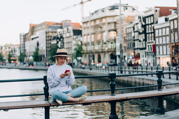 Stylish female tourist using smartphone near canal in historic district on bridge