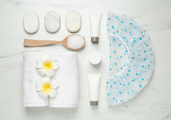 Flat lay composition with shower cap and toiletries on white marble background
