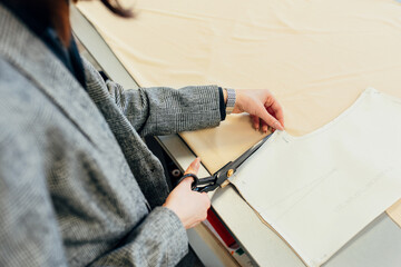 Closeup of a fashion designer's hand cutting with scissors the fabrics. Business owner woman working on a new collection in her creative office.