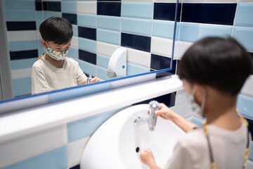 A boy is washing hand himself in the bathroom.
