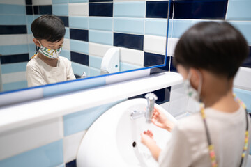 A boy is washing hand himself in the bathroom.