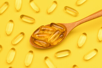 Wooden spoon with Omega 3 pills on yellow background. Supplement food vitamin D capsules. Close up...