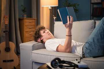A young boy with dark curly hair is lying on a couch in the living room propping his head up,...