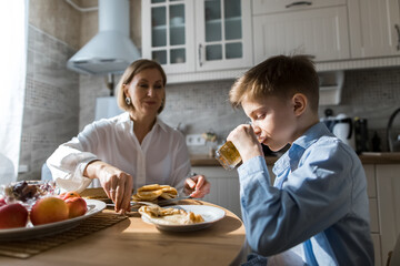 Adult woman in the kitchen treats a child with pancakes and juice.