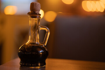 Obraz na płótnie Canvas Balsamic vinegar in a beautiful curly bottle with a wooden cork stands on the table in an italian restaurant, warm lights bokeh. Close-up