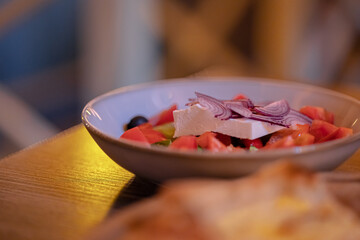 Greek salad of vegetables, tomatoes, olives, cucumbers, onions and cheese in a plate on a wooden table. Warm and cozy