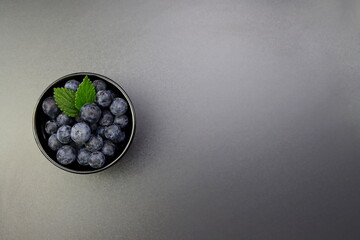 Blueberries with green mint leaves in a black round bowl on a gray background. © kati17