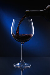 Pouring red wine from bottle into glass on color background
