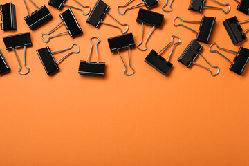 Black binder clips on orange background, flat lay. Space for text