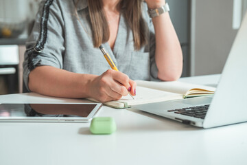 Cropped Photo of Businesswoman Working at Home Office Desk.
Unrecognizable business woman talking with coworkers on video call and writing down notes in notebook while sitting at desk with copy space.