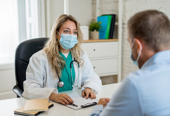 Happy female doctor and patient wearing protective face mask having a consultation in clinic office