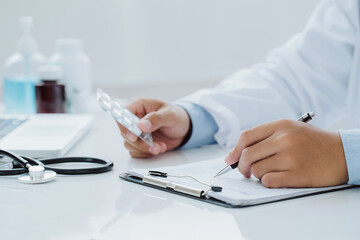 Doctor hold in one hand a blister with pills and write prescription to patient at work table. Panacea and life save prescribing treatment legal drug store concept.