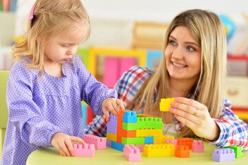 Obraz na płótnie Canvas Cute little girl and her mother playing colorful plastic blocks