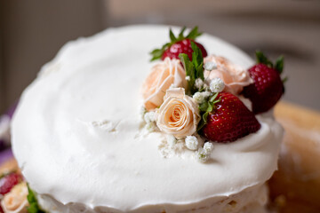 birthday cake with a decor of natural flowers and strawberries on a wooden board. vanilla biscuit, cream cheese. cake for a holiday