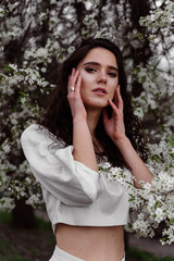 Lovely girl near blooming trees in the park. Outdoor walking in at sunny day. Lifestyle of young woman.