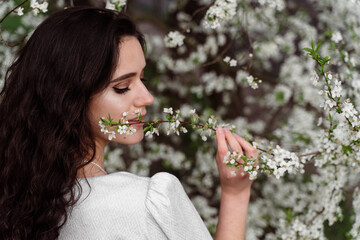 Girl touches and sniffs a branch of a white flowering tree without medical mask. Spring walking in the park.