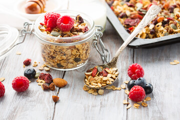 Handmade muesli granola with fresh berries, honey, seeds in glass jars on wooden white table