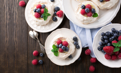 Pavlova cake dessert with fresh summer berries on wooden table.