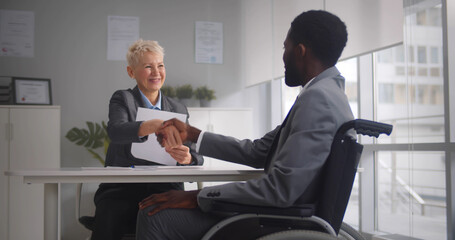 African disabled job candidate and mature female employer shaking hands and smiling at camera - Powered by Adobe