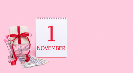 A gift box in a shopping trolley, dollars and a calendar with the date of 1 november on a pink background.