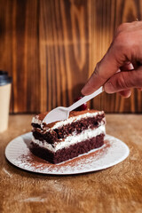 Close-up of a piece of chocolate cake with milk cream. The treat lies on disposable tableware. Takeaway food. Dessert in a cafe or restaurant.