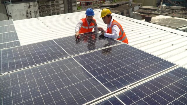 Solar power plant engineer manager training and talking to asian worker control inspecting photovoltaic on rooftop in urban city. diverse technician checking Solar Cell on High rise building outdoors
