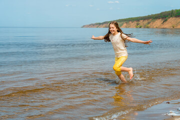 A little girl in bright yellow pants runs in the water and frolics on the beach